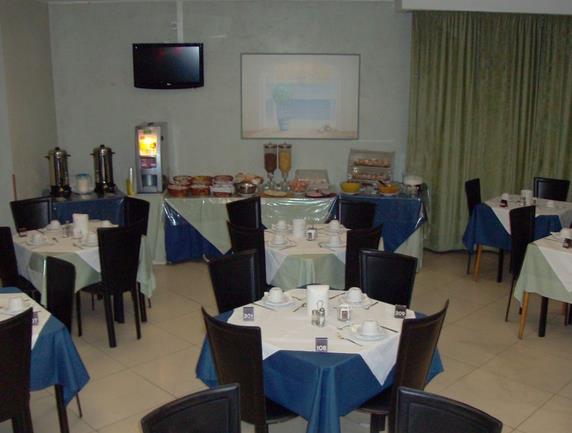 Sala restauracyjna z przygotowanymi stolikami na śniadanie i stołem bufetowym w tle.