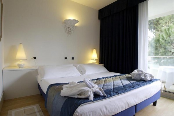 Pokój hotelowy z podwójnym łóżkiem, białą pościelą i niebieskim narzutem, obok łóżka stoją dwie lampy.