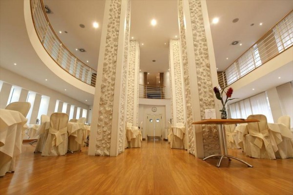 Jasna restauracja z okrągłymi stolikami i białymi krzesłami, udekorowana roślinami.