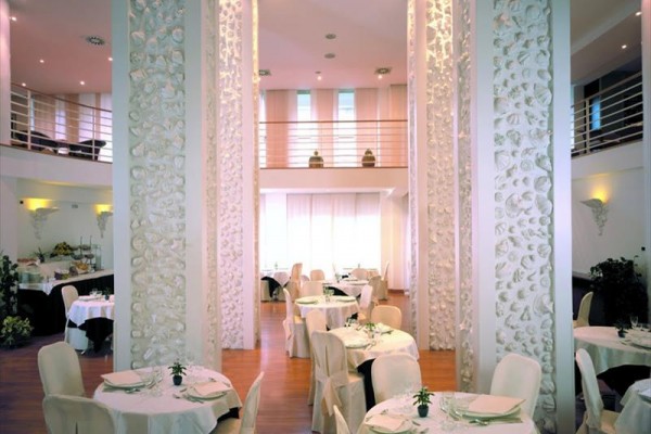 Restauracja z białymi okrągłymi stołami i ozdobnymi kolumnami.