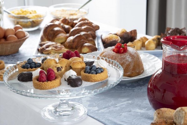 Talerz z deserami takimi jak koszyczki z owocami oraz karafka z czerwonym napojem na stole z pieczywem.