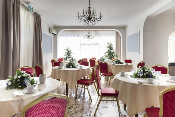 Elegancka sala bankietowa z okrągłymi stołami, czerwonymi krzesłami i aranżacjami kwiatowymi.