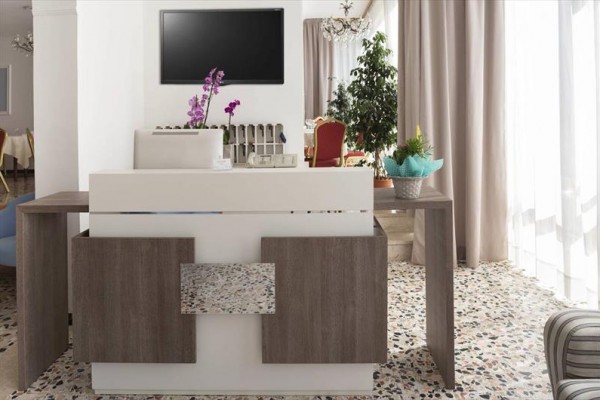 Recepcja w hotelowym holu z nowoczesnym wystrojem, kwiatami i telewizorem na ścianie.