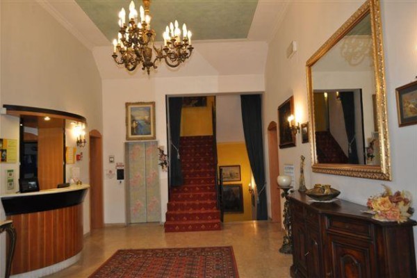 Recepcja hotelowa z żyrandolem, lustrem i czerwonym dywanem na schodach.
