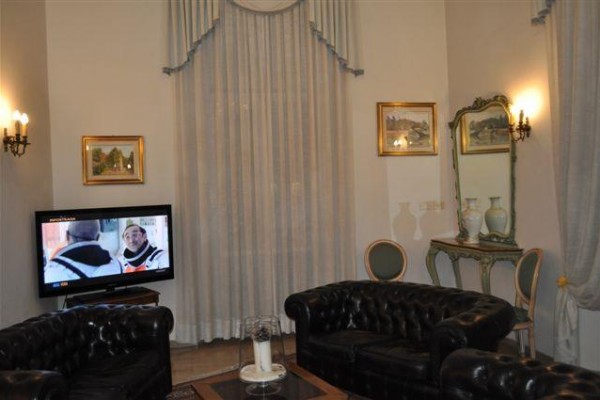 Salon z czarnymi skórzanymi sofami, telewizorem i zasłonami.