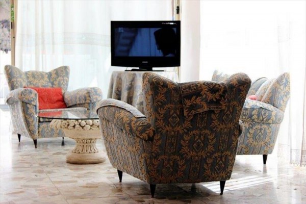Salon z niebieskimi fotelami, szklanym stolikiem i telewizorem w tle.