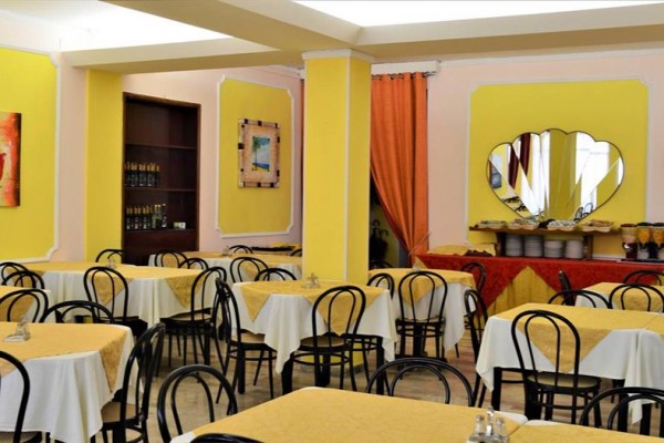 Restauracja z żółtymi ścianami, okrągłymi stołami z białymi obrusami i czarnymi krzesłami.