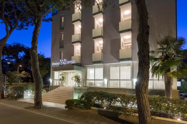 Fasada oświetlonego hotelu ze schodami i balkonami wieczorem.