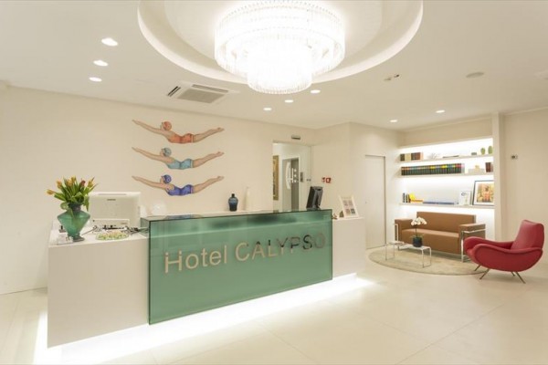 Recepcja hotelu Calypso z nowoczesnym wystrojem, obrazami pływaków na ścianie i szklanym żyrandolem.
