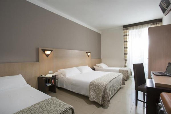 Pokój hotelowy z trzema łóżkami, stołem, krzesłami i oknem.