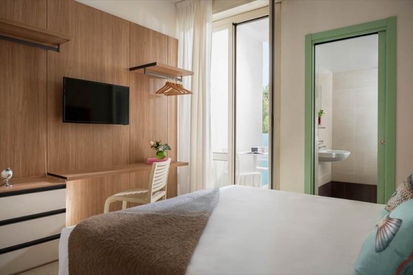 Pokój hotelowy z łóżkiem, telewizorem na ścianie, biurkiem i widokiem na łazienkę.
