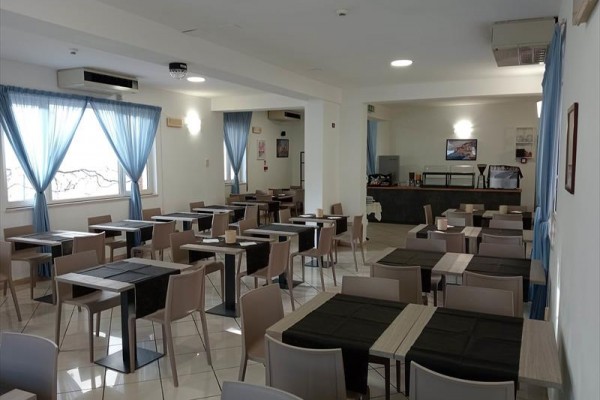 Restauracja z ustawionymi stołami i krzesłami, niebieskie zasłony w oknach.
