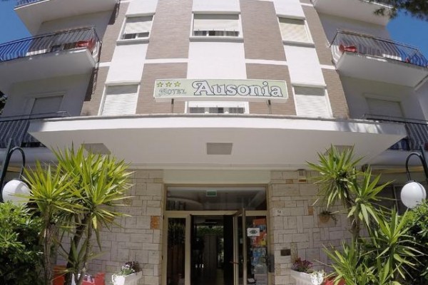 Wejście do trzypiętrowego hotelu z zielonymi roślinami wokół.