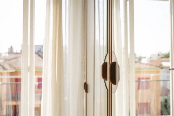 Szklane drzwi z drewnianą klamką otwarte na balkon z białymi zasłonami.