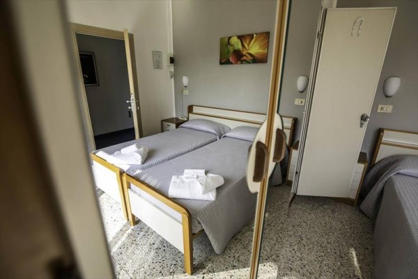 Dwa pojedyncze łóżka z szarymi narzutami i złożonymi ręcznikami na łóżkach w pokoju hotelowym.
