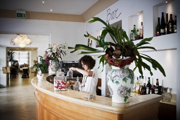 Kobieta za barem przygotowuje napoje w eleganckiej restauracji z kwiatową dekoracją.