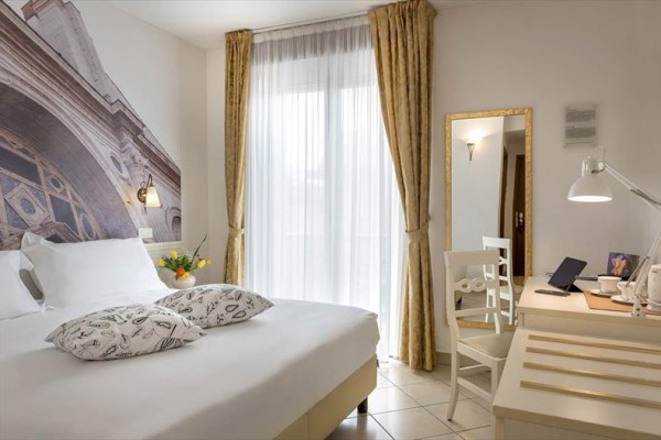 Jasny pokój hotelowy z dużym łóżkiem, biurkiem i dużym lustrem.