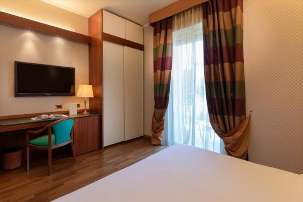Nowoczesny pokój hotelowy z pojedynczym łóżkiem, biurkiem i telewizorem na ścianie.