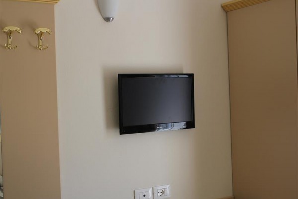 Telewizor zawieszony na beżowej ścianie między szafkami.