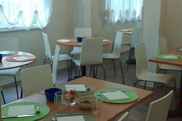 Prosto urządzona jadalnia z okrągłymi stołami i białymi krzesłami.