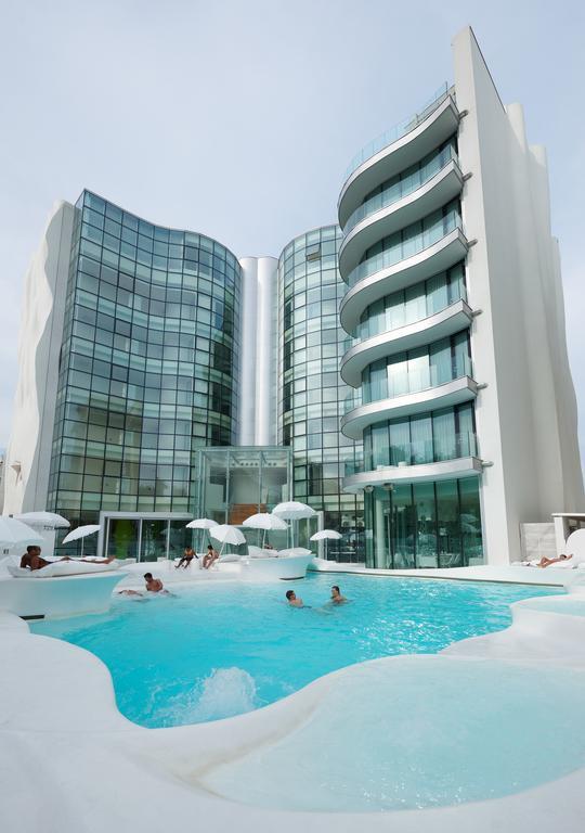 Nowoczesny hotel z basenem, wokół którego rozmieszczone są leżaki i parasole.