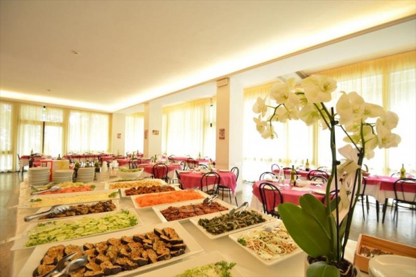 Restauracja z dużymi oknami, stołem bufetowym pełnym jedzenia i orchideą na pierwszym planie.