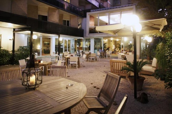 Zewnętrzne miejsca do siedzenia z drewnianymi stołami i krzesłami na oświetlonym tarasie ogrodowym restauracji.