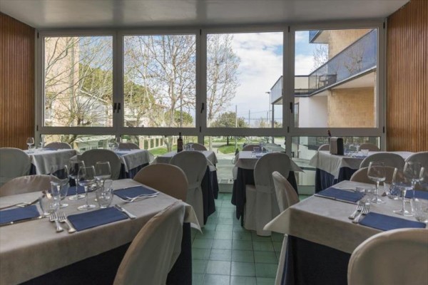 Restauracja z nakrytymi stołami i dużymi oknami z widokiem na ogród.