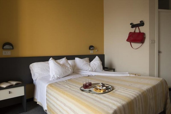 Łóżko małżeńskie z śniadaniem na tacy w pokoju hotelowym z jedną otwartą książką na stoliku nocnym.
