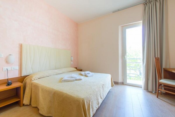 Pokój hotelowy z podwójnym łóżkiem i otwartymi drzwiami na balkon.