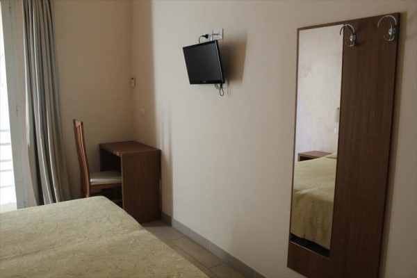 Pokój hotelowy z łóżkiem, krzesłem przy stole, lustrem i telewizorem na ścianie.