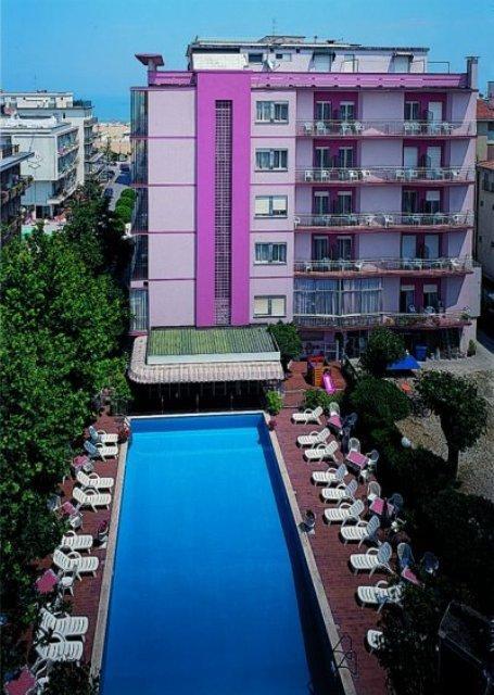 Różowy hotel z basenem i leżakami wokół.