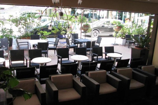 Na zewnątrz na tarasie restauracji znajdują się puste stoły i krzesła z widokiem na parking.  