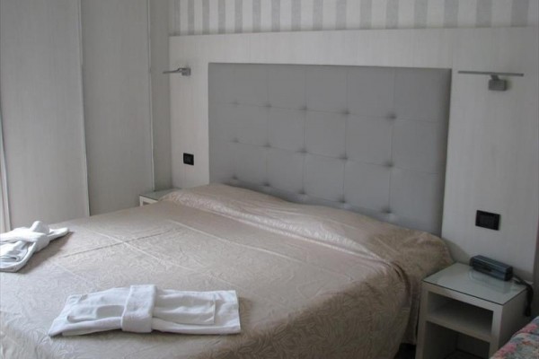 Jasny pokój hotelowy z łóżkiem małżeńskim i białą pościelą.