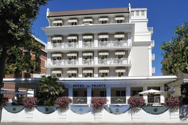Biało-niebieski hotel z balkonami, kwiatami i napisem 