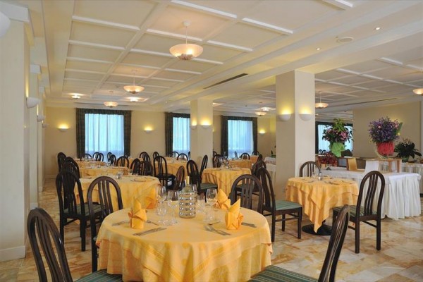 Restauracja z okrągłymi stołami, żółtymi obrusami i drewnianymi krzesłami.