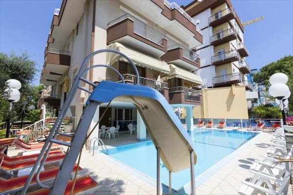 Hotelowy basen z niebieską zjeżdżalnią i leżakami.