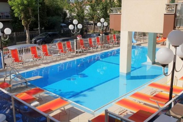 Basen otoczony czerwonymi leżakami i lampami na tarasie hotelu.