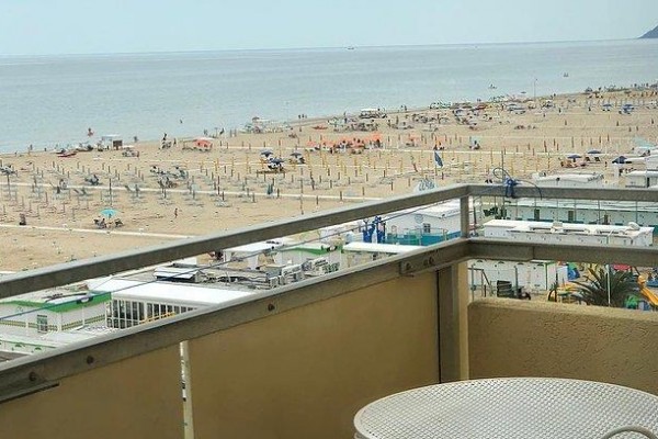 Widok z balkonu na plażę z leżakami i morze w tle.