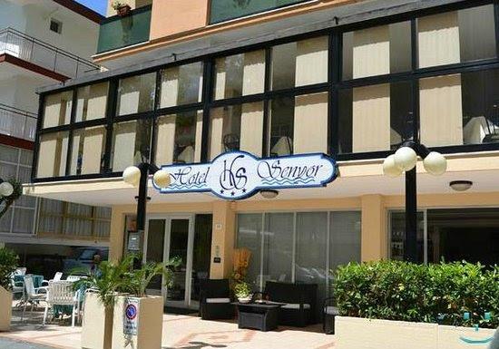 Wejście do hotelu z szklaną elewacją i zewnętrznym miejscem do siedzenia.