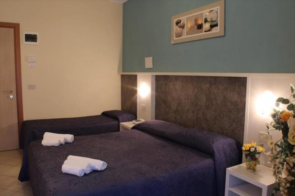 Pokój hotelowy z dwoma łóżkami, oświetleniem na ścianie i dekoracyjnymi kwiatami.