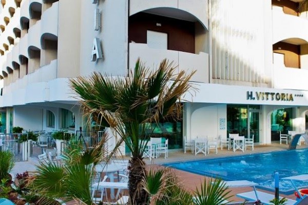 Nowoczesny hotel z szklanym ogrodzeniem i małym basenem przed wejściem.