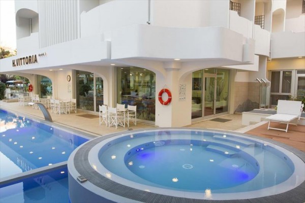 Zewnętrzny basen z jacuzzi przy hotelu z tarasem wyposażonym w białe krzesła i stoliki.