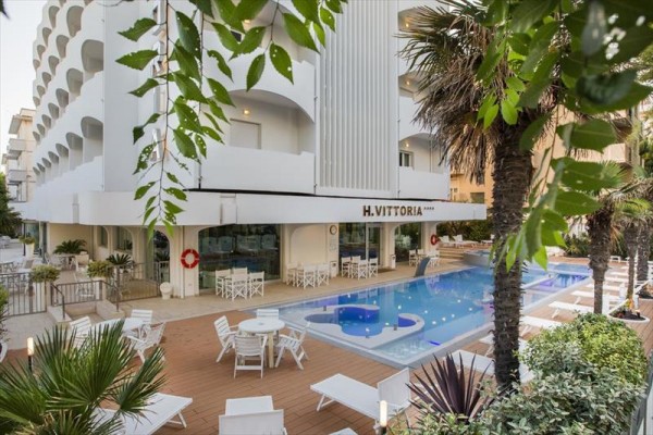 Basen przed nowoczesnym budynkiem hotelu z zielenią wokół.