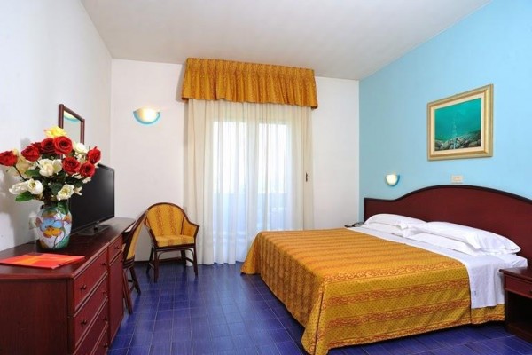 Pokój hotelowy z łóżkiem małżeńskim, krzesłem i komodą z lustrem.