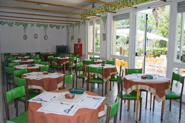 Restauracja z okrągłymi stołami, zielonymi krzesłami i nakryciami obok dużych okien z widokiem na zewnątrz.