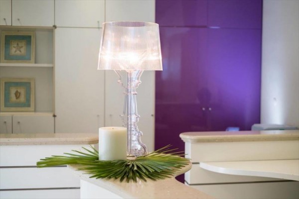 Przezroczysta lampa stołowa i świeca na blacie z dekoracją z liści palmowych.