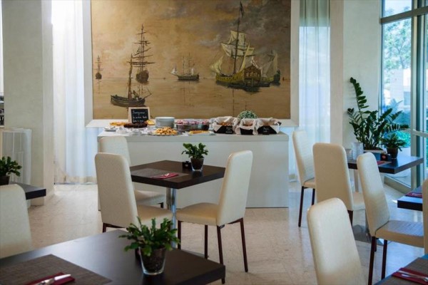 Wnętrze restauracji z malowidłem statków na ścianie i stołami z białymi krzesłami.