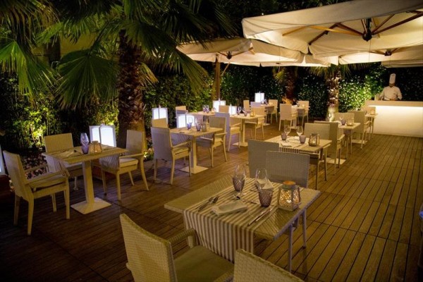 Zewnętrzna restauracja z drewnianymi stołami i krzesłami pod białymi parasolami.