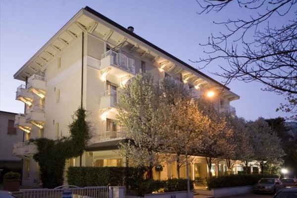 Budynek hotelowy z oświetlonymi balkonami i kwitnącymi drzewami na pierwszym planie.